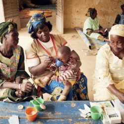 Three women help administer malaria medication to a child